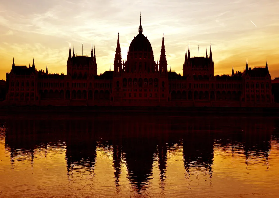 Ungarisches Parlamentsgebäude in Budapest im warmen Gegenlicht mit Spiegelung in der Donau.