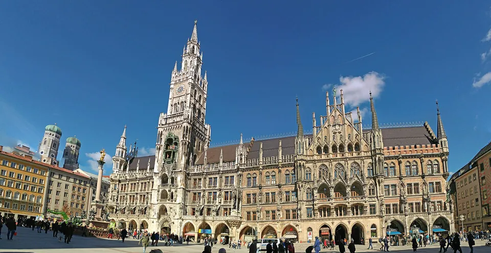 Neues Rathaus am Münchner Marienplatz mit den Türmen der Frauenkirche unter blauem Himmel.