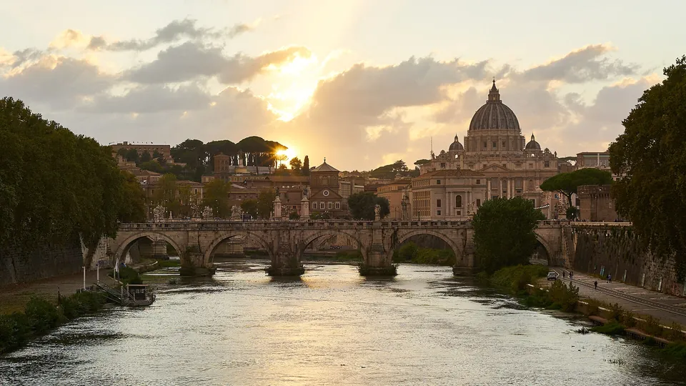Ponte Sant’Angelo über dem Tiber mit dem Petersdom im warmen Abendlicht.