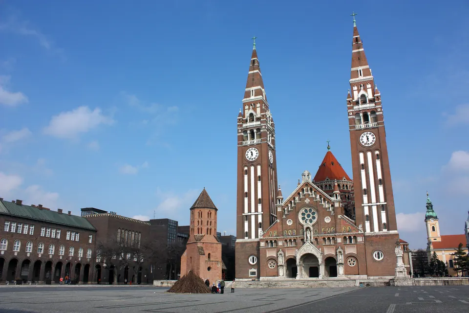 Domplatz in Szeged mit der zweitürmigen Votivkirche und dem Dömötör-Turm bei Tageslicht.